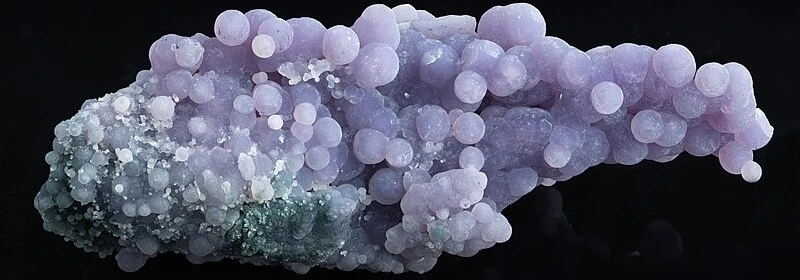 This is a picture of a grape agate that is a pleasantly pale purple color. The picture was taken against a black background.