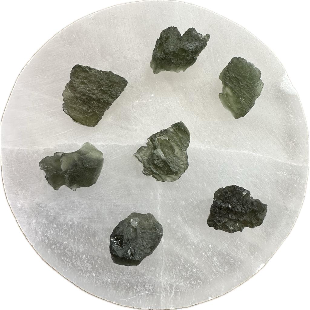 Moldavite tektites displayed on a selenite mineral charging disc. Moldavite is only found in the Czech Republic