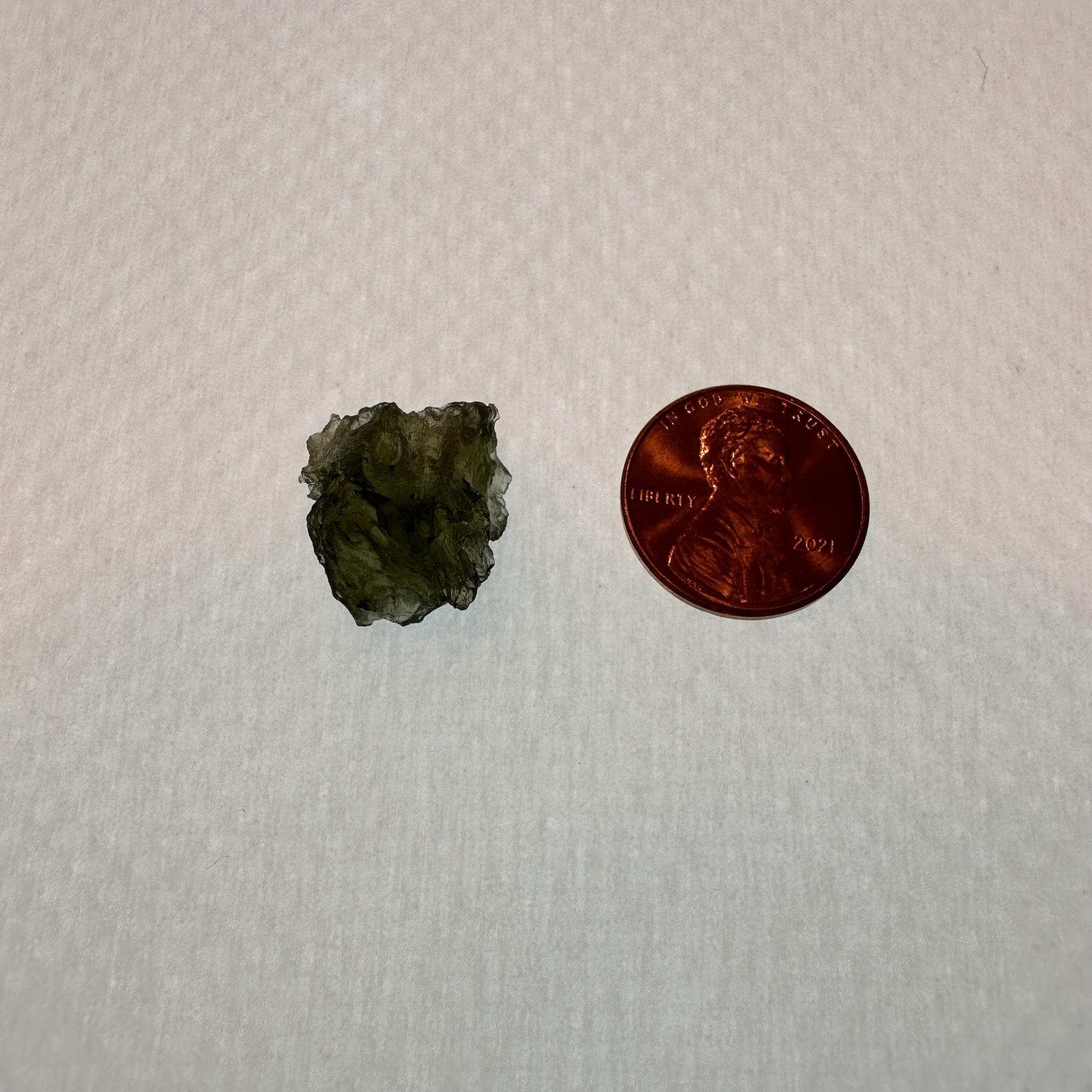 A beautiful green Moldavite, next to a penny to show the size of the actual mineral